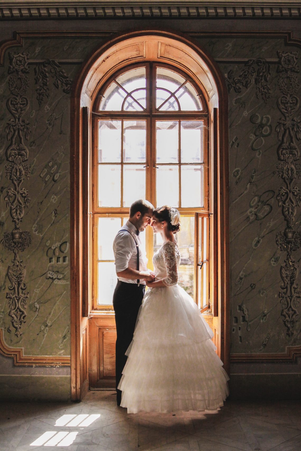 Dobrý svadobný fotograf - nevesta so ženíchom pred starobylým oknom